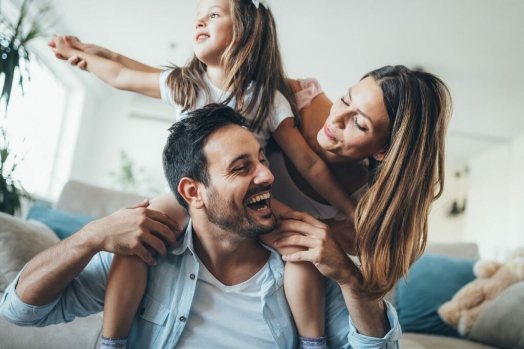 girl on dad's shoulders with mom smiling at dad